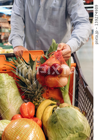 Cabbage, tomatoes, bananas in the shopping cart. Close up view of man that is in the grocery store 139274989