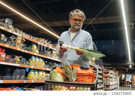 Smartphone is in hand. A senior man is buying food in the grocery store Smartphone is in hand. A senior man is buying food in the grocery store 139275005