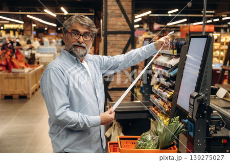 Shocked by the huge check. A senior man is buying food in the grocery store Shocked by the huge check. A senior man is buying food in the grocery store 139275027