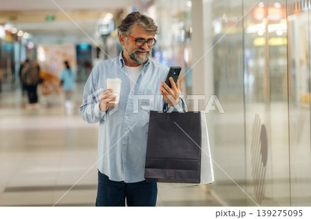 Cup of drink and smartphone are in hands. Senior man is in the mall, shopping time conception 139275095