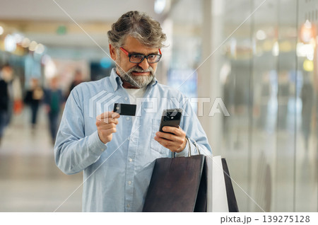 Process of online payment by using credit card and smartphone. Senior man is in the mall, shopping time conception Process of online payment by using credit card and smartphone. Senior man is in the mall, shopping time conception 139275128