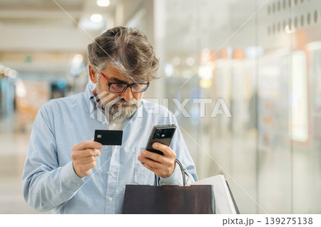 Online payment by using credit card and smartphone. Senior man is in the mall, shopping time conception Online payment by using credit card and smartphone. Senior man is in the mall, shopping time conception 139275138