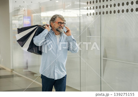 Usage of the smartphone. Senior man is in the mall, shopping time conception Usage of the smartphone. Senior man is in the mall, shopping time conception 139275155