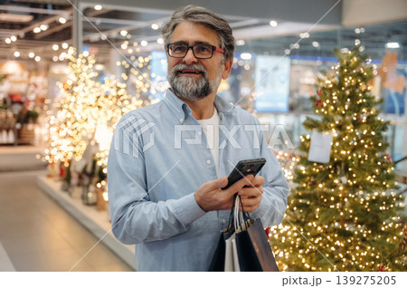 Holidays time, against decoration, with phone. Senior man is in the mall, shopping time conception Holidays time, against decoration, with phone. Senior man is in the mall, shopping time conception 139275205