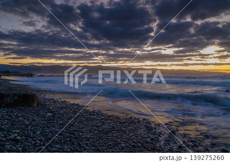 Twilight waves crash on rocky shore as clouds dance over the horizon in a coastal paradise 139275260