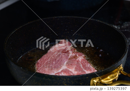 Sizzling beef steak heating in a black frying pan on a modern kitchen stovetop during evening preparation 139275397