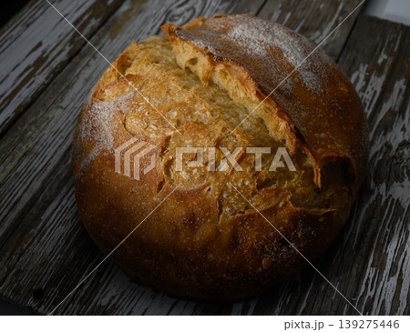 Artisan loaf resting on rustic wooden surface in warm light showcasing its texture and golden crust 139275446