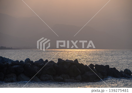 Sunset reflections over tranquil waters with rocky shoreline near distant mountains Sunset reflections over tranquil waters with rocky shoreline near distant mountains 139275481
