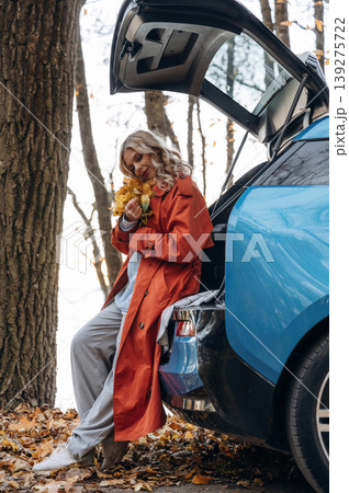 Beautiful blonde woman is with her blue electric car on the road of forest Beautiful blonde woman is with her blue electric car on the road of forest 139275722