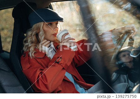 Hot drink in white cup. Happy blonde woman is sitting her electric car Hot drink in white cup. Happy blonde woman is sitting her electric car 139275750