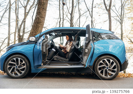 On the road, door opened, parked. Beautiful woman is sitting in her electric car On the road, door opened, parked. Beautiful woman is sitting in her electric car 139275766