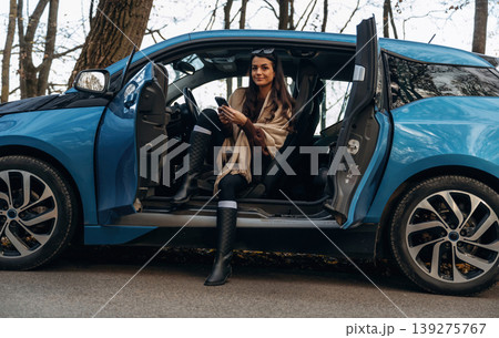 On the road, door opened, parked. Beautiful woman is sitting in her electric car 139275767