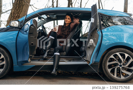 On the road, door opened, parked. Beautiful woman is sitting in her electric car 139275768