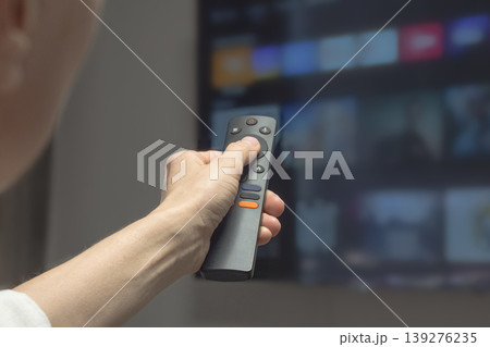 Hand holds remote, aiming at glowing TV screen. Smart TV. Hand holds remote, aiming at glowing TV screen. Smart TV. 139276235