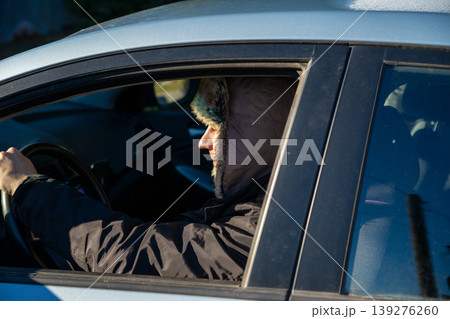 Man driver in winter hat driving car. Delivery worker during cold season. Transportation service or taxi driver on city road. Safe travel and professional vehicle operation in wintertime. Man driver in winter hat driving car. Delivery worker during cold season. Transportation service or taxi driver on city road. Safe travel and professional vehicle operation in wintertime. 139276260