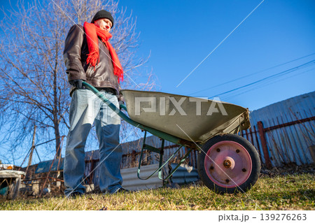 Man holding empty wheelbarrow in garden during autumn. Gardener preparing for yard work. Seasonal outdoor maintenance, land improvement and landscaping concept on sunny day. Man holding empty wheelbarrow in garden during autumn. Gardener preparing for yard work. Seasonal outdoor maintenance, land improvement and landscaping concept on sunny day. 139276263