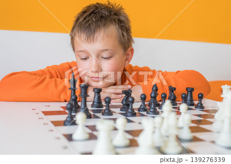Cute child boy playing chess at school indoors Cute child boy playing chess at school indoors 139276339