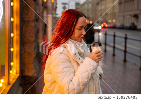 Woman holding a coffee cup while standing under neon lights on a rainy evening in the city. wellness, unity with oneself 139276485
