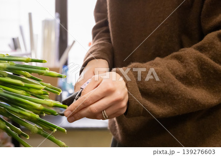 Florist cutting flower stems with scissors. Woman preparing bouquet in flower shop. Small business concept. Professional floral arrangement and gardening workshop for spring holiday. 139276603