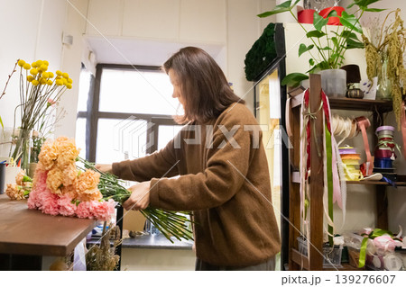 Woman florist arranging bouquet with fresh carnation flowers in floral shop. Professional girl worker creating botanical composition in studio. Small business and floral design concept. Woman florist arranging bouquet with fresh carnation flowers in floral shop. Professional girl worker creating botanical composition in studio. Small business and floral design concept. 139276607