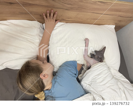 Beautiful child and cat pet sleeping together in bedroom. Girl 10 years old and hairless kitten 139276732