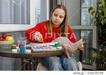 Cute child girl painting and sitting with cat pet on the terrace. 139276746