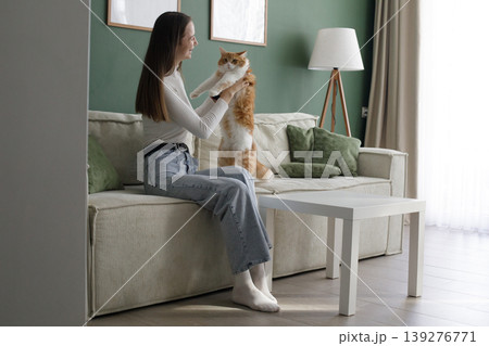 Joyful woman and cat sitting on a couch in a living room Joyful woman and cat sitting on a couch in a living room 139276771