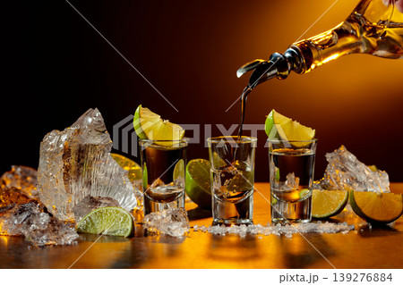 The tequila is poured from the bottle into shot glasses. 139276884