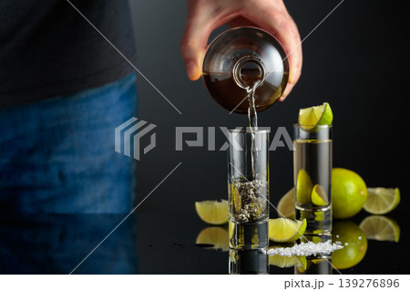 Tequila shots with salt and lime slices on a black reflective background. 139276896