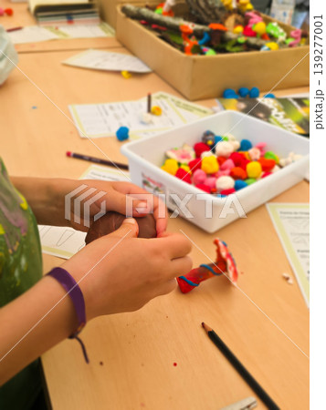 A child molds colorful clay into a mushroom shape at a classroom desk. Concepts of creativity, tactile learning, and child development through play. 139277001