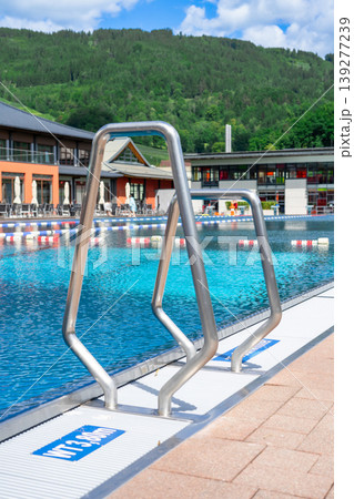 Handrails of stairs in an outdoor public swimming pool with turquoise water Handrails of stairs in an outdoor public swimming pool with turquoise water 139277239