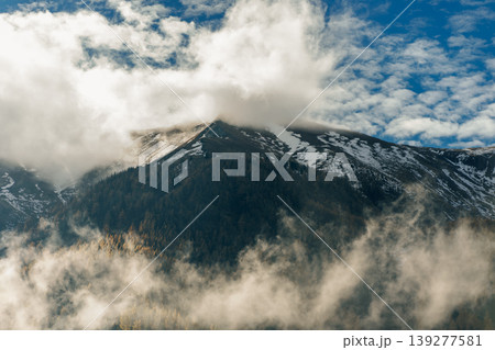 Peak of the Alps covered with dense forest and sparse snow among thick clouds 139277581