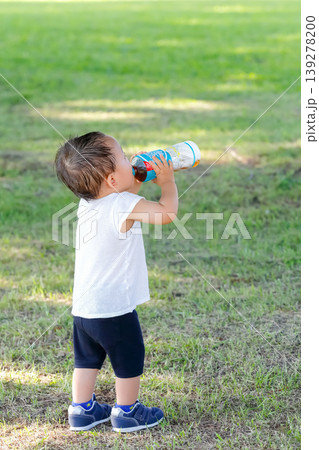 芝生の広場で水分補給する幼児の全身姿_縦 139278200