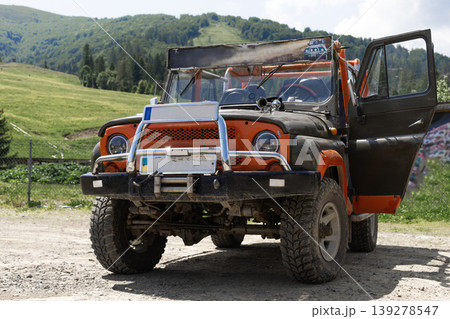 Old customized offroad vehicle with open door parked on dirt road in green mountains. 139278547