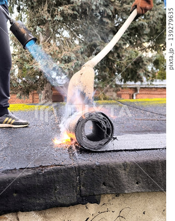 Laying rolled waterproofing on a roof using a gas torch 139279635