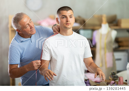 Elderly man tailor takes body measurements from young man 139281445