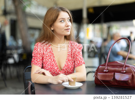 Pretty young woman relaxing and drinking coffee sitting on street cafe in day 139281527