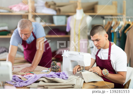 Young guy sews on machine male assistant drawing pattern Young guy sews on machine male assistant drawing pattern 139281553