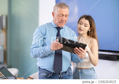 Mature man discussing a new work project with female employee, they look at the tablet Mature man discussing a new work project with female employee, they look at the tablet 139281623