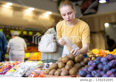 Woman chooses ripe kiwi for purchase in greengrocer shop Woman chooses ripe kiwi for purchase in greengrocer shop 139281695