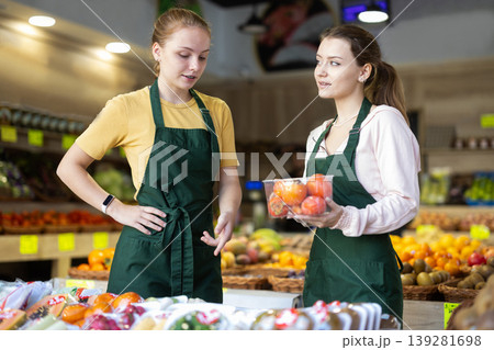 Two female salespeople display persimmons and mangoes in grocery supermarket display case Two female salespeople display persimmons and mangoes in grocery supermarket display case 139281698