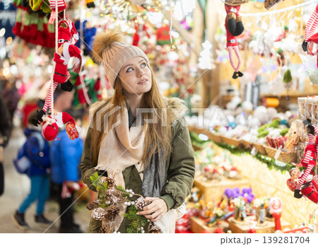 Young woman in souvenir store examines Christmas cloth toys and figurines Young woman in souvenir store examines Christmas cloth toys and figurines 139281704