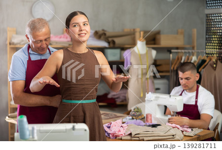 Mature man tailor takes measurements from girl client, guy work with sewing machine 139281711