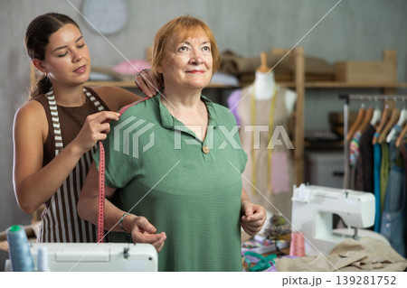 Young seamstress takes measurements from mature woman Young seamstress takes measurements from mature woman 139281752