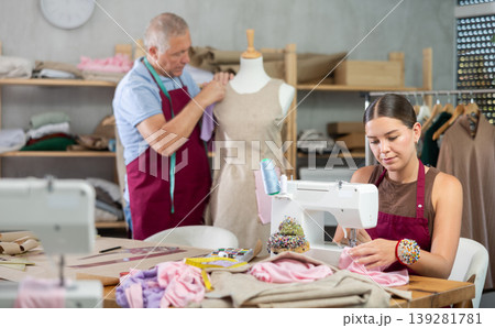 Young woman sews on machine male assistant sews on mannequin Young woman sews on machine male assistant sews on mannequin 139281781