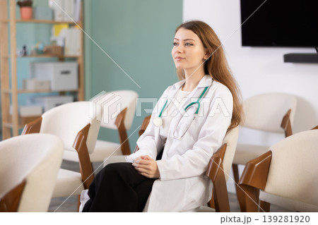 Portrait of young female intern dressed in white coat and with stethoscope listening at lesson in university 139281920