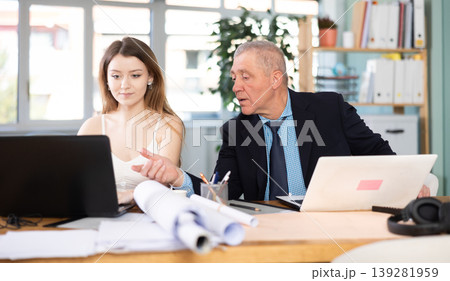 Mature man working in office, sitting at desk next to woman Mature man working in office, sitting at desk next to woman 139281959