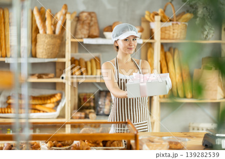 Girl entrepreneur owner of bakery holds out cardboard box with pastries in hand 139282539