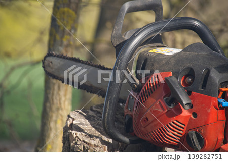 Close-up of a red and black chainsaw resting on a weathered tree stump outdoors Close-up of a red and black chainsaw resting on a weathered tree stump outdoors 139282751