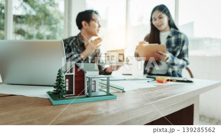 Real estate agents review documents with house model and laptop on desk in bright office, home buying or property investment consultation. Real estate agents review documents with house model and laptop on desk in bright office, home buying or property investment consultation. 139285562